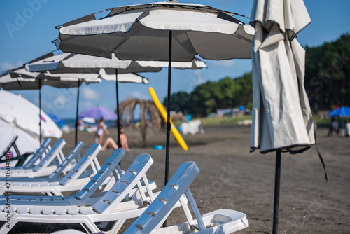Cuadro en lienzo Empty white sun loungers on a dark sand beach