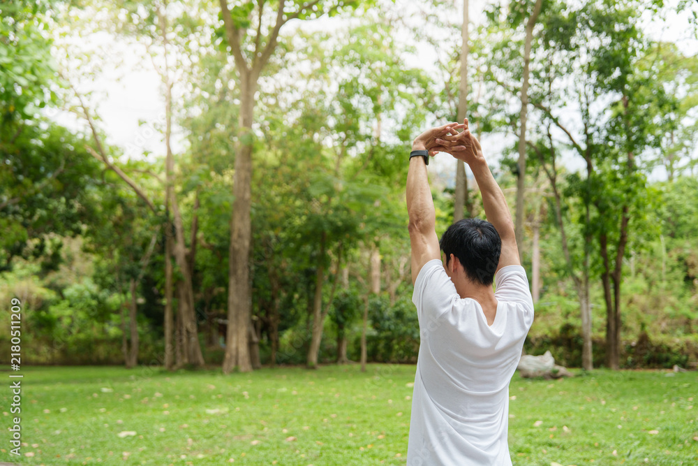 Obraz premium Asian man stretching arms overhead in green park for outdoor workout routine