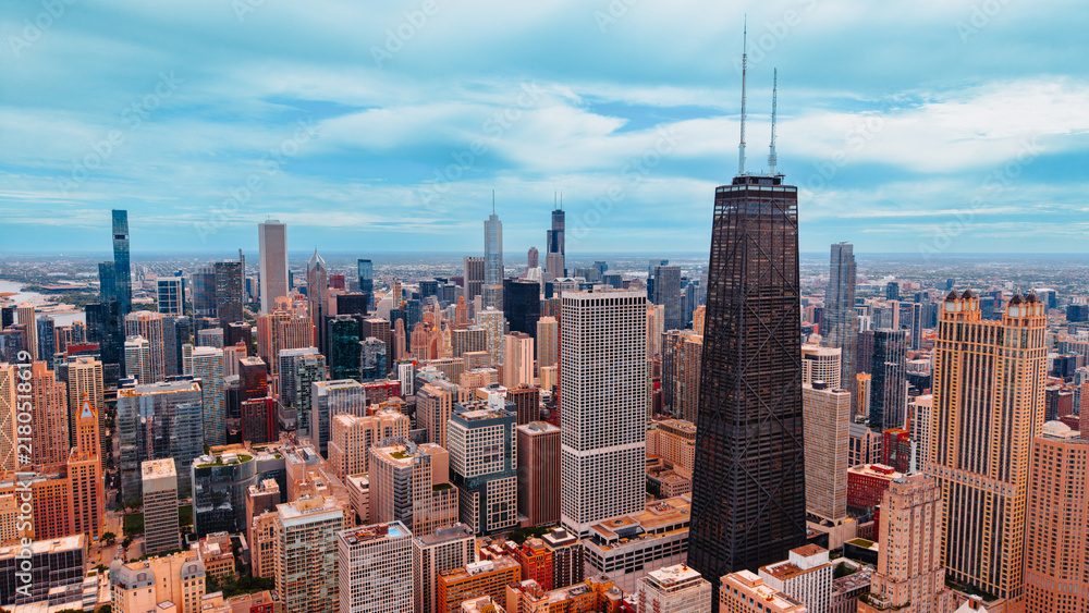 Obraz premium John Hancock Center and Chicago skyscrapers view. Aerial photograph of dark tall tower with antennas standing among modern office buildings under blue sky.