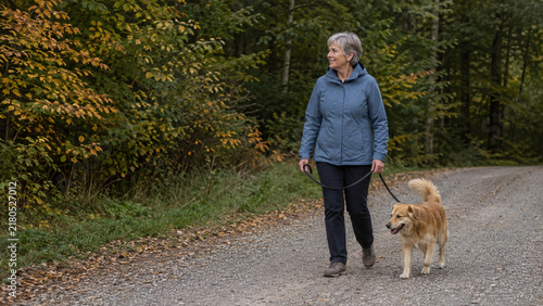 Senior woman walking a dog on an autumn park path