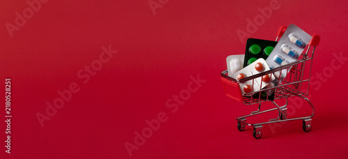 Canvastavla Mini shopping cart filled with blister packs of pills on a vibrant red background, symbolizing healthcare, pharmacy, and pharmaceutical shopping