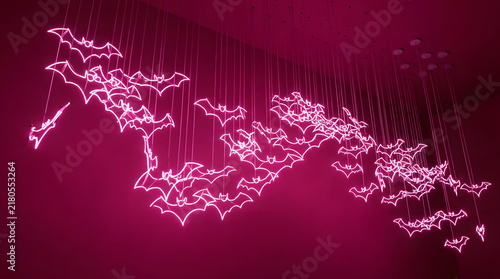Pink neon bats suspended in midair form a glowing artistic installation. Modern and playful design blending Halloween symbolism with futuristic style