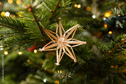 Étoile artisanale en paille suspendue au sapin de Noël avec guirlande lumineuse en bokeh