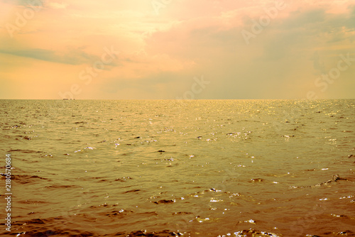 Beautiful golden sunset over the calm sea waves. The sun shines through the clouds, reflecting on the ocean surface. Peaceful nautical landscape with a warm orange and yellow vintage color palette.