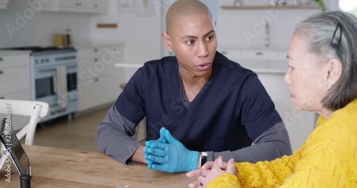 African American caregiver in scrubs seeing meter, showing sugar test to senior Chinese in kitchen
