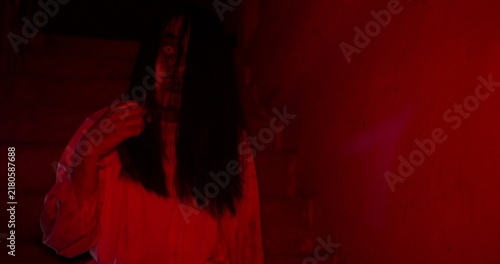 Фотография A terrifying ghost woman with a scary disfigured face haunts a dark basement, lit by an ominous red light for a Halloween horror movie scene