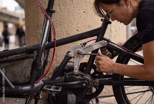 Woman bicycle mechanic repairing an electric cargo bike with an allen wrench outdoors