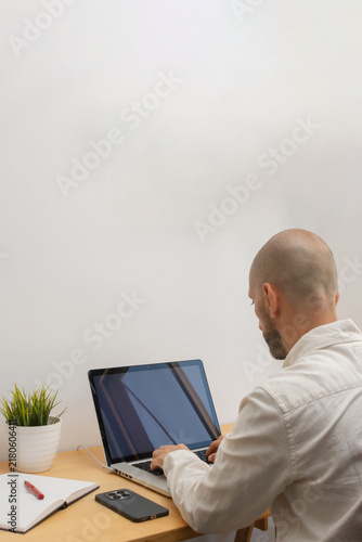 Vertical rear view of man typing on laptop at wooden desk