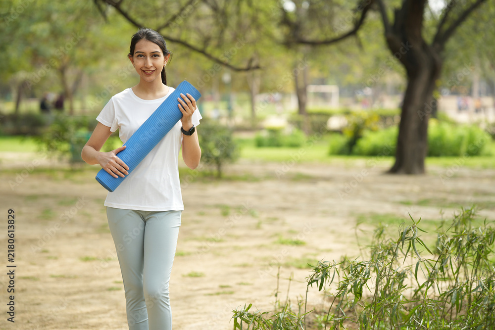 Obraz premium Indian young girl holding yoga matt while standing at park