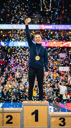 Happy Female Champion Holding Gold Medal On Podium With Confetti Falling