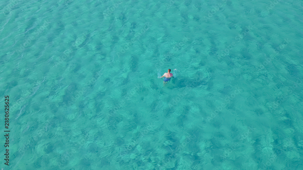 Fototapeta premium Man swimming in clear turquoise waters of Elafonisi beach, Crete, during summer, showcasing vibrant aquatic environment and natural beauty of the Mediterranean region