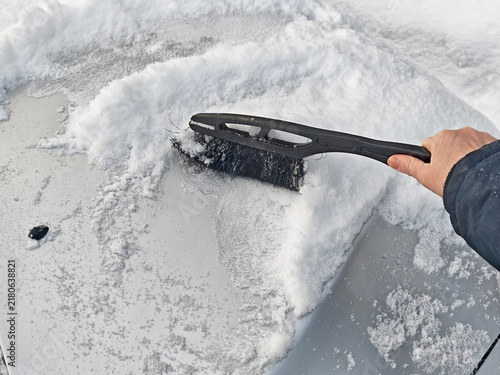 Person removes snow from a car window in winter weather during the early morning hours