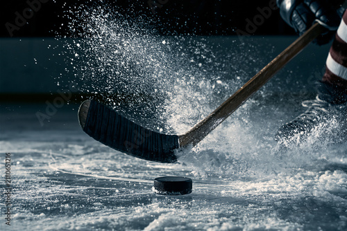 Close-up of a hockey stick blade striking a puck with ice spray frozen mid-motion, cool dramatic rink lighting, dynamic action composition with ice spray detail, intense mood. AI gen
