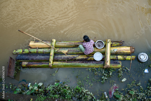 Konstfotografi resident washing utensils while sitting on a makeshift banana raft in a flood-af