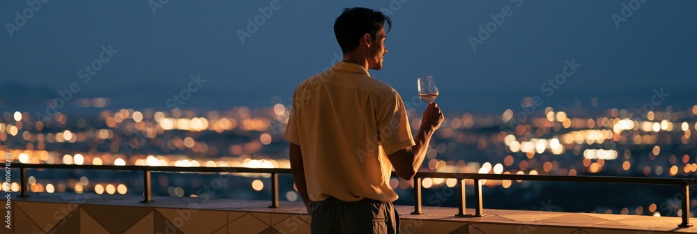 Obraz premium Man holding a wine glass on a rooftop terrace at night city skyline background for banner and wallpaper design