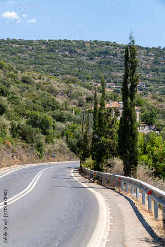 Winding asphalt road with barrier guardrail leading through green mountain landscape in Greece