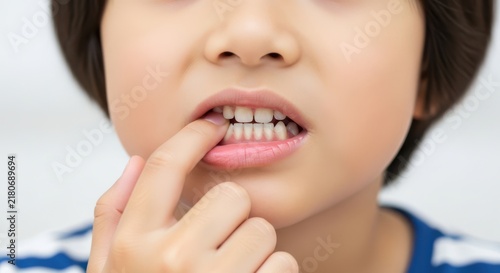 Close up of a young child touching their teeth with a finger showing dental hygiene and oral health care awareness