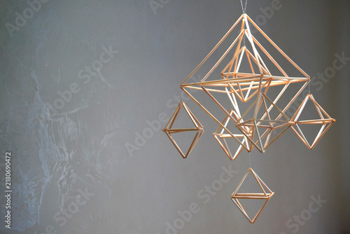Abstract geometric straw sculpture hanging with shadow cast on wall