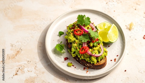 This dish features avocado spread on toast, garnished with lime, chili, and cilantro. It is served on a simple plate against a light background