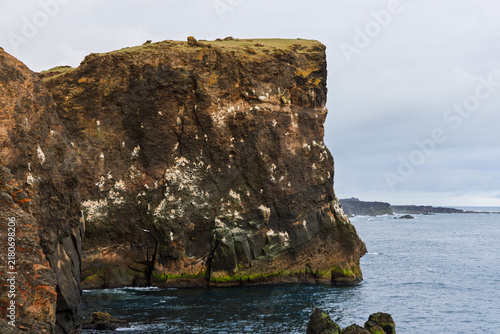 Serrated coastal rock rises above foaming water at Valahnukamol on the Reykjanes Peninsula, Iceland. Multiple ridges recede toward the horizon in flat evening light beneath overcast maritime sky.