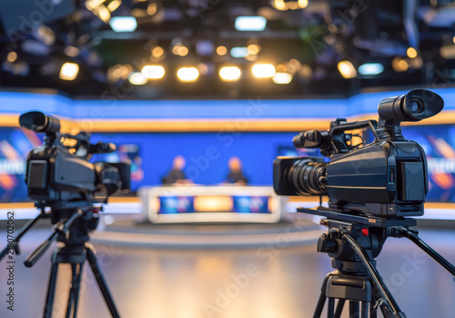 Video Camera On Tripod In Broadcasting Studio With Blurred Lights Background