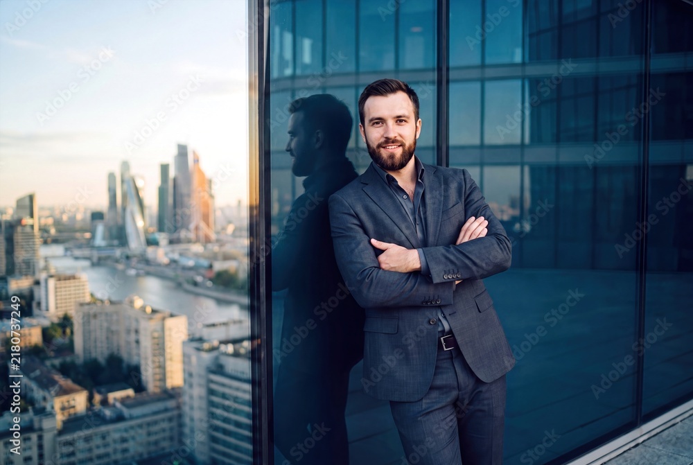 Fototapeta premium Confident Young Businessman in Elegant Suit Standing on High Rise Balcony with Modern Cityscape View