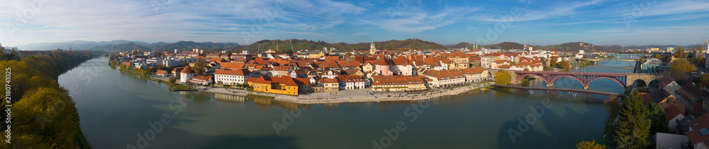 Fototapeta premium Aerial panoramic view of Maribor, Slovenia, with the historic old town, Drava River, Old Bridge, riverside promenade and surrounding hills.