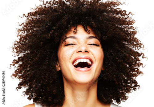 Joyful woman with vibrant curly hair laughing with closed eyes and open mouth showing happiness for positive emotions.
