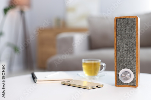 Modern audio speaker, mobile phone, cup and notebook on white table in room, selective focus