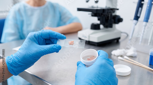 Lab technician places a tissue sample on a glass slide near a microscope for clinical biopsy analysis