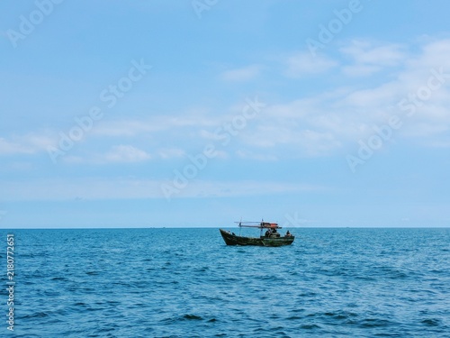 Small wooden fishing boat sailing on calm blue ocean under clear bright sky during peaceful summer day
