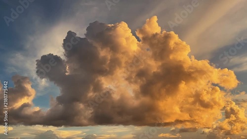 Timelapse of a massive cumulus cloud changing shape during golden hour sunset. Dramatic cloud formation illuminated by warm sunlight against a blue sky background