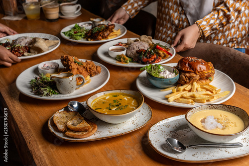 Quadro su tela High-angle view of an abundant table spread featuring a chicken burger, French fries, fried chicken, soup with toast, and rice platters