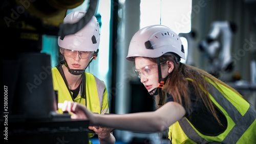 Two female robotics engineers in an R and D lab troubleshoot an artificial intelligence cobot. They are inspecting the robotic system hardware and programming.