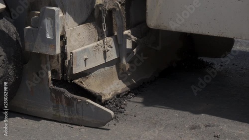 A cold milling machine removes old asphalt pavement in a tight side view, with milled fragments collecting beneath the cutter housing during road resurfacing.