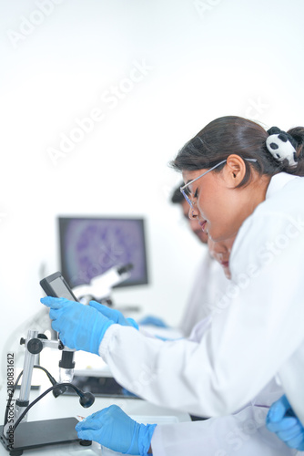 Fotografie Five laboratory colleagues gather around notes and a digital tablet in a clean research facility while wearing white lab coats and blue protective gloves and modern scientific innovation
