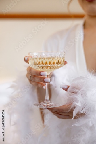 Bride holding crystal champagne coupe glass in white feather robe