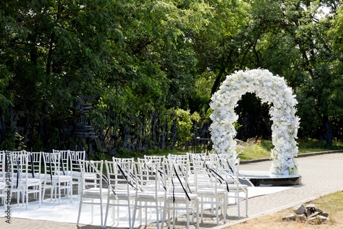 Outdoor wedding ceremony venue with white flower arch and chiavari chairs