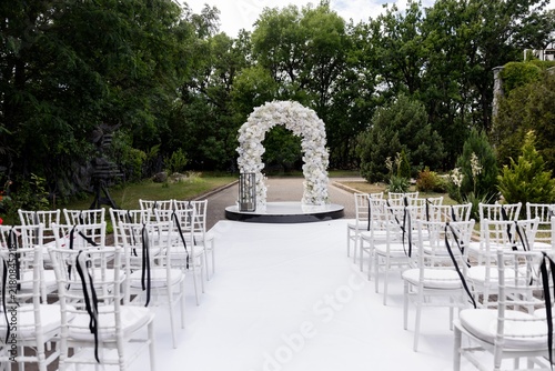 Outdoor wedding ceremony venue with white flower arch and chiavari chairs