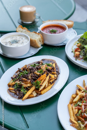 Canvastavla High-angle view of a bistro table filled with loaded beef gravy fries, chili cheese fries, bowls of hot soup with toast, and a latte coffee