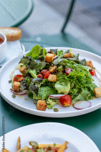 Obraz na plátne Vibrant medium shot of a gourmet garden salad filled with crispy croutons, cherry tomatoes, and sliced radish served on an outdoor café table