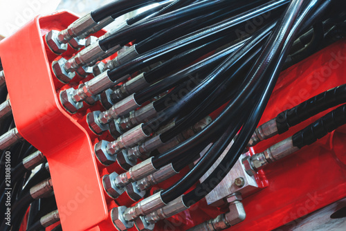 Сlose-up of black hydraulic hoses. Metal fittings connect to white cylinder. Steel beams form factory backdrop. Industrial equipment components, tech industrial technology background