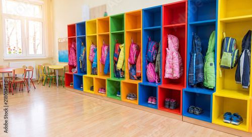 Spacious preschool corridor featuring rows of bright colorful lockers filled with hanging children coats and jackets illuminated by natural sunlight from window