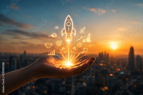 Rocket icon glowing above an open hand represents business startup and growth over a city skyline at sunset.