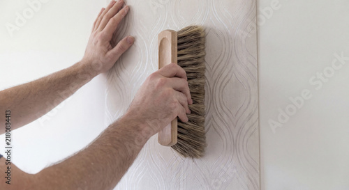 Close up shot of worker hands using wooden smoothing brush to flatten freshly hung patterned wallpaper onto wall surface