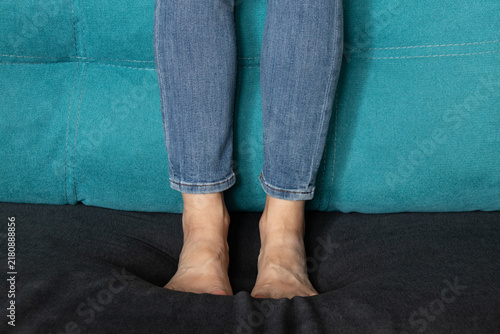 Bild auf Leinwand A woman's bare feet in jeans are standing on a sofa at home