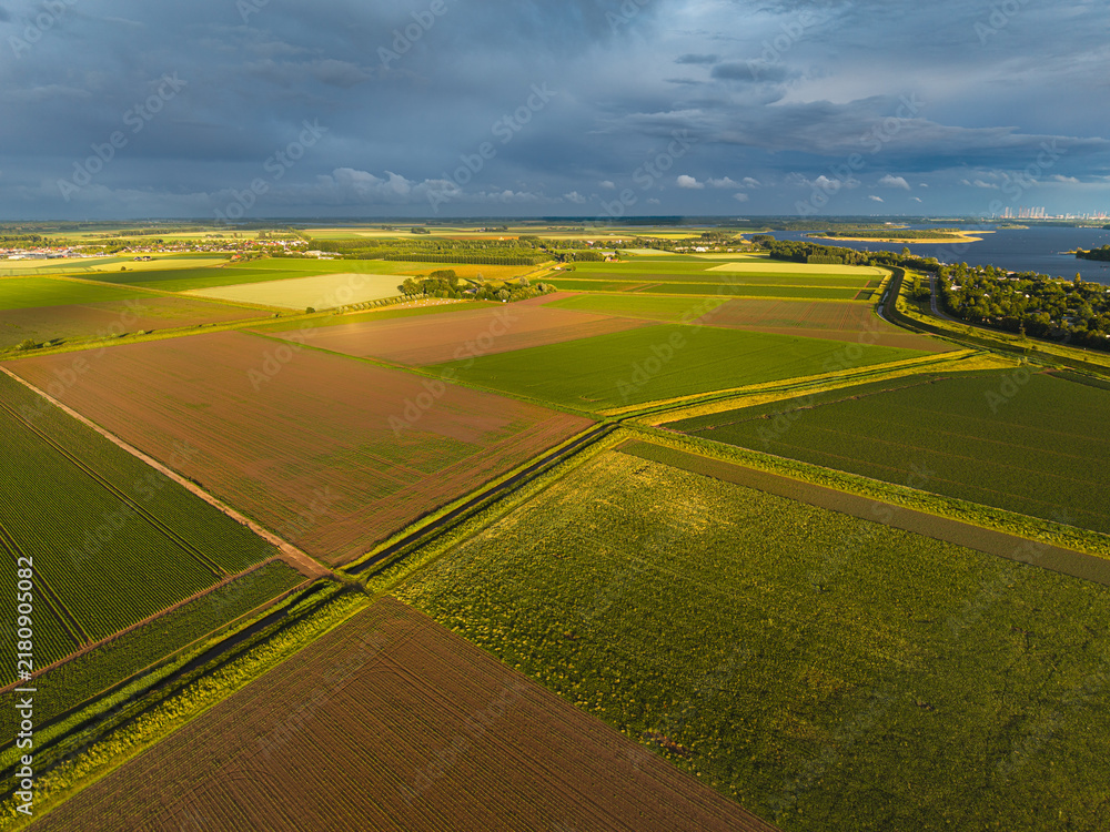 Obraz premium High angle wide horizontal aerial drone photograph of polder fields, drainage canals, Lake Veere, and storm sky in Kamperland, Zeeland, Netherlands in golden hour summer sunlight