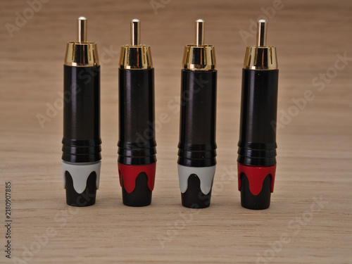 Bild auf Leinwand Four RCA Plugs on Wooden Surface - Four audio RCA phono plugs with gold-plated connectors and color-coded boots are neatly arranged on a light brown wooden table