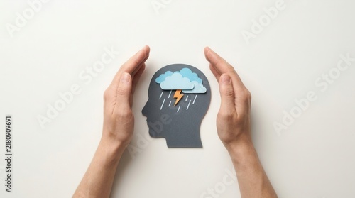 A mental health concept showing inner turmoil and care with hands protecting a head silhouette containing stormy weather.