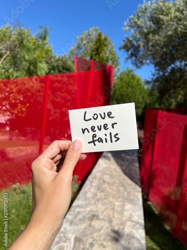 Love never fails - hand with vertical christian card on red background